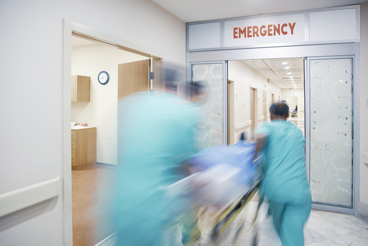 3 doctors rushing a patient in a hospital bed into the emergency department of a hospital. The doctors are blurred as they are running.