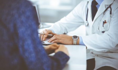 Doctor with white coat and patient with blue jacket having a conversation, with the doctor taking notes