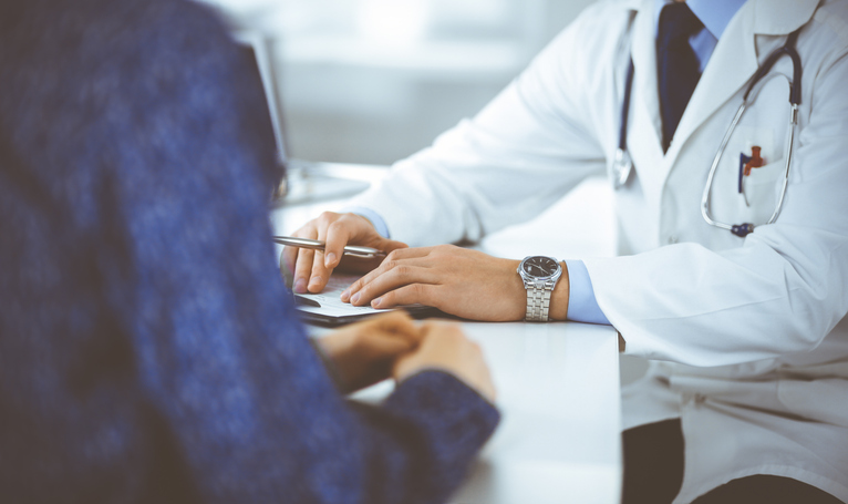 Doctor with white coat and patient with blue jacket having a conversation, with the doctor taking notes