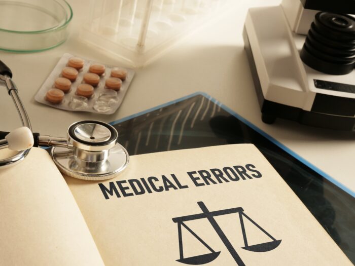 Open book displaying the text "medical errors" and legal scales alongside a stethoscope and tablets.