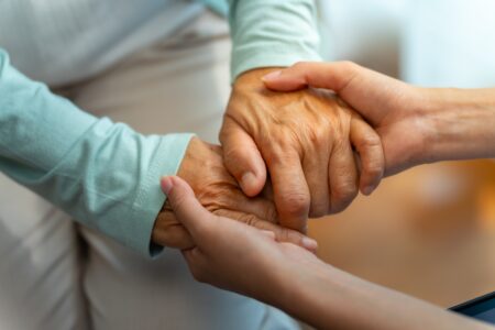 A close image of a doctor holding a patients hands in a comforting fashion.