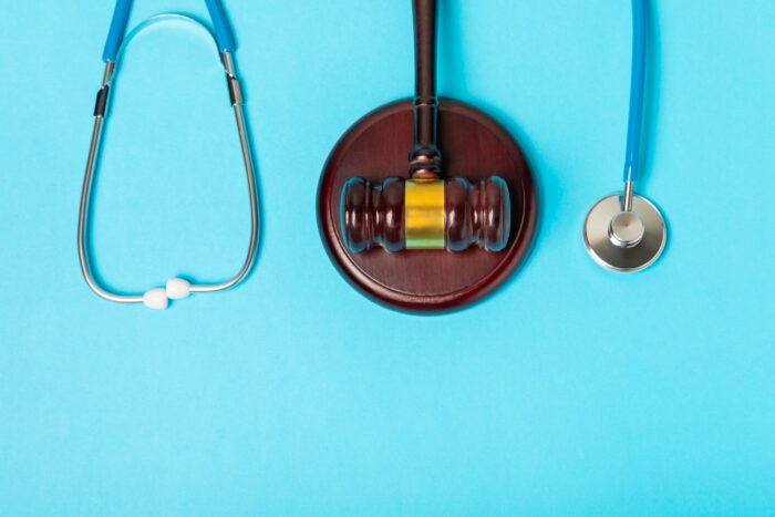 A light blue background with a gavel in the centre and a stethoscope laid down beside it.