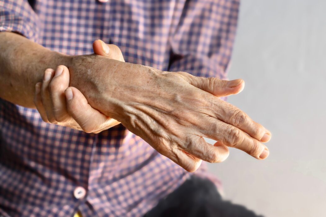 An elderly man with his right hand out in front of him, his left hand is holding his wrist indicating pain.